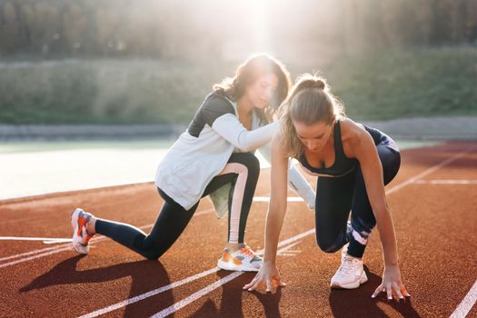 Caucasian Athlete ready to start. Young female runner with personal trainer preparing for blasting off in mist on sports track of stadium, training before competition. Sportswoman. Cardio exercises.