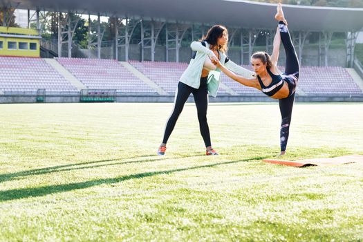 Fitness female in sportswear with trainer training outdoor stretching body at morning. Physiotherapist worker doing treatment to his client. Girl doing exercises under physiotherapist supervision.