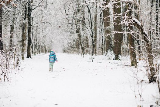 Cute child girl in a colorful clothing running in a snowy winter park . Little winter girl in fairy ice forest. Walk in winter forest.