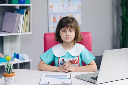 Funny little girl looking at camera are sitting on the couch at home. Cute kid child with pretty face. Concept of a happy childhood. Portrait of girl in medic uniform looking at camera