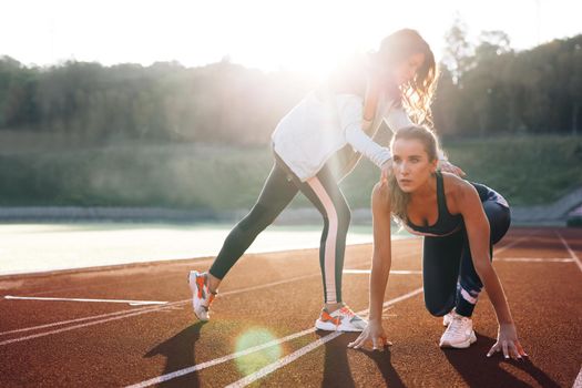 Female athlete training with personal trainer at running track in the morning light. Active fitness woman runner jogging in sunny track summer day outdoors. Jogger activity. Sportswoman.