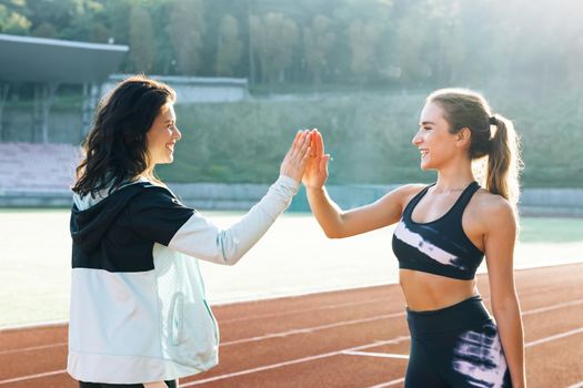 Two happy attractive young sportswomen giving high five after training. Sportswomen relaxing after jogging in park.