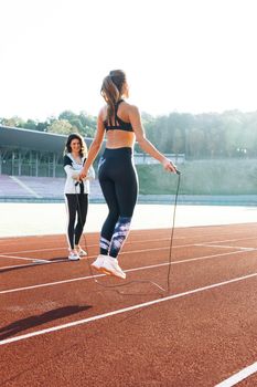 Woman with personal trainer jumping rope as part of her fitness workout. Sporty female with a good figure jumps rope on sports track of stadium. Exercising strength cardio and power.