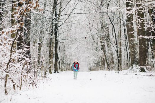 Little happy girl in winter clothes is having fun running in snowy winter day. Happy child girl plays with a snow in winter day. Girl enjoys winter, frosty day.