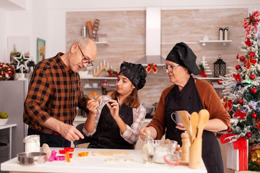 Happy family cooking traditional gingerbread dessert making homemade dough using baking tree shape in xmas decorated kitchen. Grandchild enjoying christmas holiday together preparing cookies