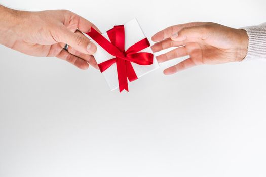 Beautiful holiday or Christmas background image of a Caucasian male's hand giving a small red ribbon wrapped gift box to a mixed race African American woman wearing a sweater with copy space.