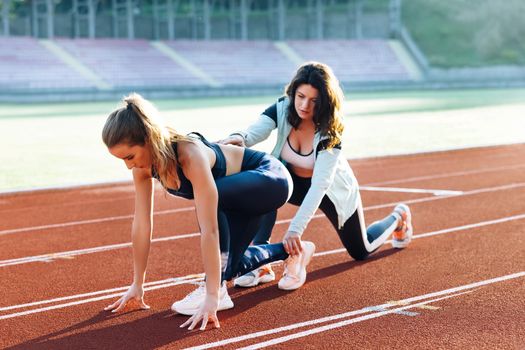 Active fitness woman runner jogging in sunny track summer day outdoors. Female athlete training with personal trainer at running track in the morning light. Jogger activity. Sportswoman.