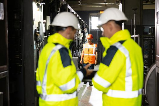 Back View of Two Engineers Stand in Electric Power Station, Use Digital Tablet Computer, Have Discussion. Energy Business Technology Industry Concept