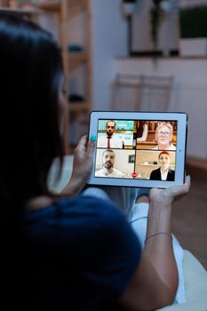 Having online meeting using tablet laying on comfortable sofa at home. Remote worker having online meeting consulting with colleagues on video conference and webcam chat using internet technology.