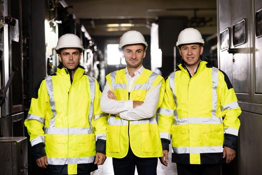 Workers wearing safety uniform and hard hat on unfocused background. Portrait of group of professional telecommunication industry engineers smiles and looks at the camera.
