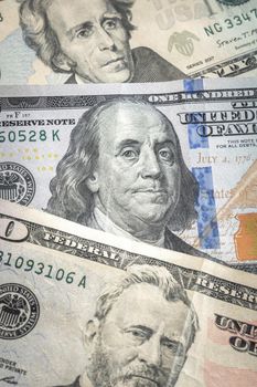 A Benjamin or a United States hundred dollar bill lays between a twenty and a fifty dollar bill or paper currency fanned out on a table for a economic or business background.