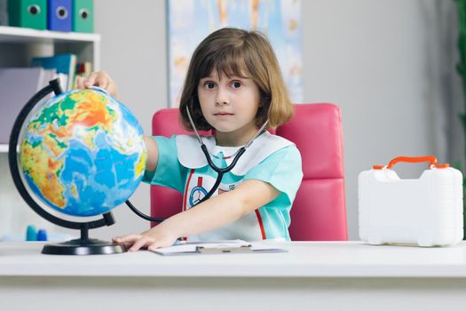 Little girl is dressed in medical clothes with a stethoscope in her hands examines and plays a game of healing the planet Earth. World planet earth eco friendly. Sick earth planet Covid-19 symptoms