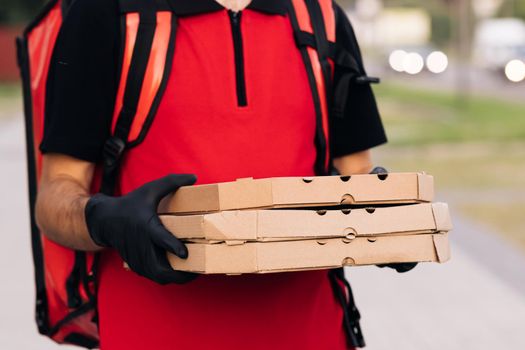 Delivery man holding three pizza cardboard boxes at city street, food deliveryman in protective medical face mask, gloves, Coronavirus COVID-19 epidemic quarantine outbreak. Delivery services