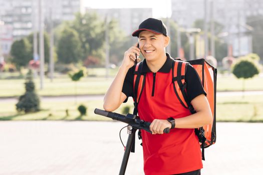 Male courier with isothermal food case box arrives to the entrance to the house and calls for client. Food delivery guy with red backpack deliver orders.