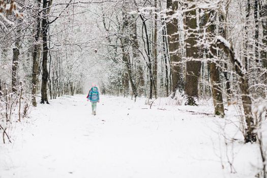 Child girl in a colorful clothing running in a snowy winter park . Little winter girl in fairy ice forest. Walk in winter forest. Expressing positivity, true brightful emotions, smiling.