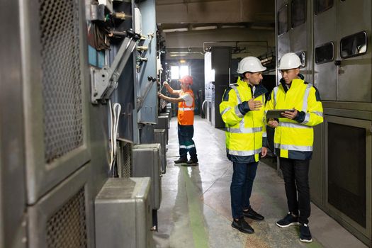 Male Electrical Engineers in Hard Hats Discuss New Project while Using Tablet Computer. They're Making Calculated Engineering Decisions. They Work at the Electric Power Factory.