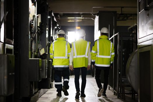 Back view of group multiethnic team of industrial engineers walking in manufacturing plant discussing new project or production plan. Inspectors supervising electric power station.