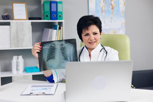 Female doctor in white medical coat making conference call on laptop computer, consulting distance patient online in video chat, explain treatment by webcam concept