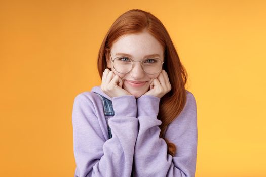 Lovely cute redhead sweet silly girl geek university student wearing glasses lean hand smiling tenderly look affection adore listen sensual confessions boyfriend, standing orange background.