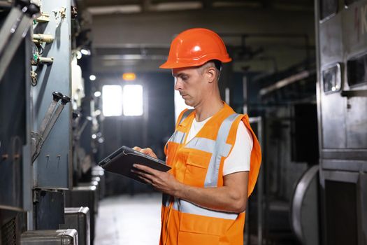 Professional Male Heavy Industry Engineer Wearing Safety Uniform and Using Tablet Computer. Industrial Specialist Standing in a Metal Construction Manufacture.