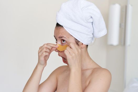 After a shower, the girl is wrapped in a towel and wears cosmetic patches for the skin under the eyes. Cosmetic procedures at home.