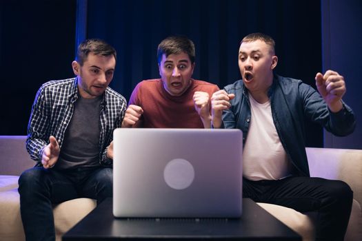 Male friends watching online football game match at laptop. Men fans buddies supporters cheering celebrating victory goal score support winning team. Men watching football in streaming on laptop.