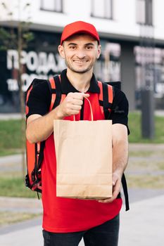 Food delivery man order from a restaurant. Handsome young man in a T-shirt and a cap. Happy delivery worker holding packet with food smiling. Delivery service door to door.