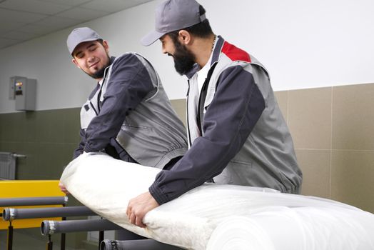 Men workers packing carpet in a plastic bag after cleaning it in automatic washing machine and dryer