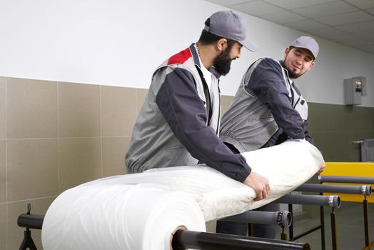 Men workers packing carpet in a plastic bag after cleaning it in automatic washing machine and dryer