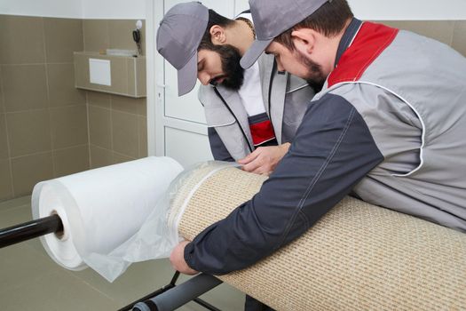 Men workers packing carpet in a plastic bag after cleaning it in automatic washing machine and dryer