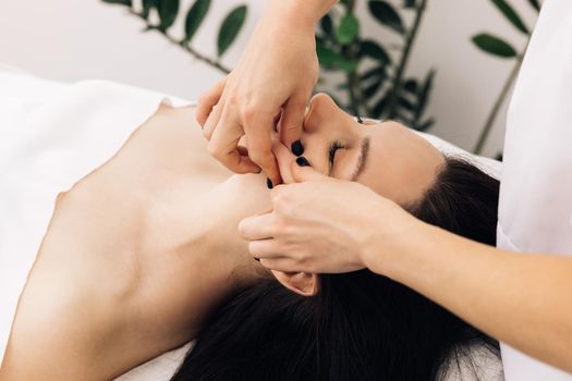 Face Massage in beauty spa salon. Female enjoying relaxing face massage in cosmetology spa centre. Body care, skin care, wellness, beauty treatment. Spa woman facial Massage.