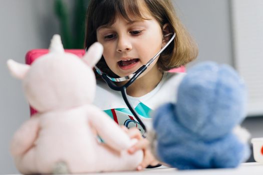 Cute preschool girl kid wearing medical uniform, listening to pets breathing, parrots and toy patients. Child playing hospital game pretending to be doctor, veterinarian, doctor treat homeless animals