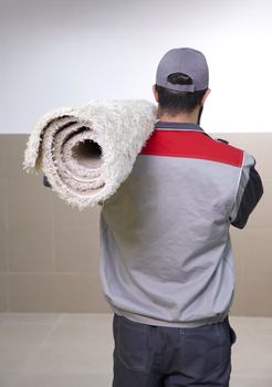 Man wearing a uniform standing with a roll of carpet on his shoulder