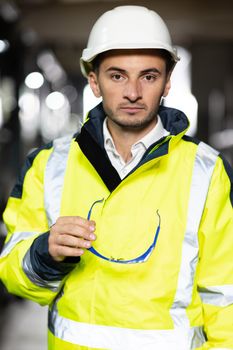 Professional Heavy Industry Engineer Worker Wearing Uniform, Glasses and Hard Hat in a Steel Factory Looks at Camera. Caucasian Industrial Specialist Standing in a Metal Construction Manufacture.