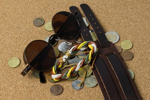 sun glasses with various bracelets and coins rest casually on the light brown leather on a flat surface