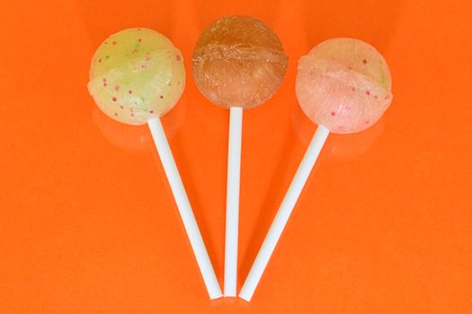 Set of lollipops on orange background. Big bright tasty lollipops on white sticks on orange background with copy space. Sweet candy concept.