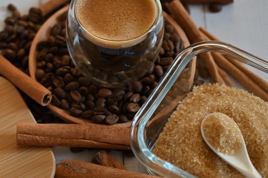 a glass glass stands on coffee beans in a wooden plate next to a sugar bowl with brown sugar close up