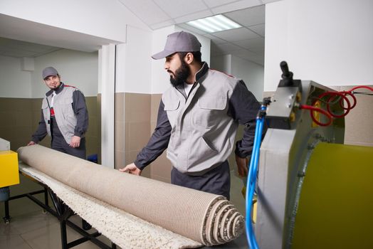 Men workers cleaning get carpet from an automatic washing machine and carry it in the clothes dryer in the Laundry room