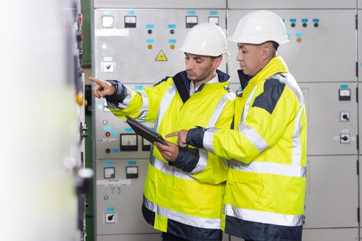 Electrical engineers checking control panel board with tablet. High voltage power station. Electrical engineers standing near therminal box of solar panel.