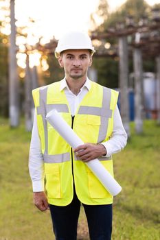 Successful Contractor Investor Architectural Engineer Wearing Hard Hat and Safety Vest Standing on a Commercial Building Construction Site, Crosses Arms Confidently Hold Blueprint in his Hand.