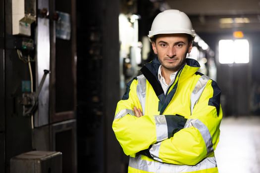 Portrait of young factory engineer or worker wearing safety vest and hard hat crossing arms at electrical control room . Industry and engineering concept.