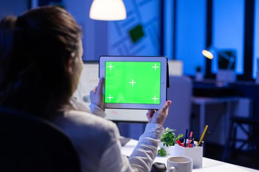 Manager woman holding tablet with green screen monitor during online web conference. Entrepreneur looking at desktop monitor display with green mockup, chroma key sitting at desk in business office