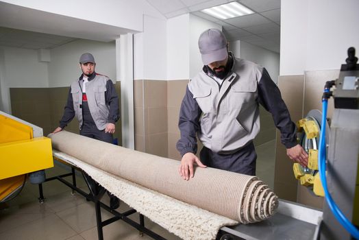 Men workers cleaning get carpet from an automatic washing machine and carry it in the clothes dryer in the Laundry room