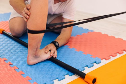 Adult male physiotherapist treating the foot of a female patient. Woman with elastic bandage on knee doing sport exercises in gym. Physio gives myotherapy using trigger points on athlete woman