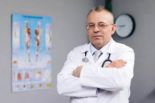 Confident Thoughtful Senior Adult Male Professional Medic, Old Doctor Wears White Medical Coat Glasses Holding Stethoscope Looks at the Camera in Hospital Office. Healthcare and Medicine Concept.