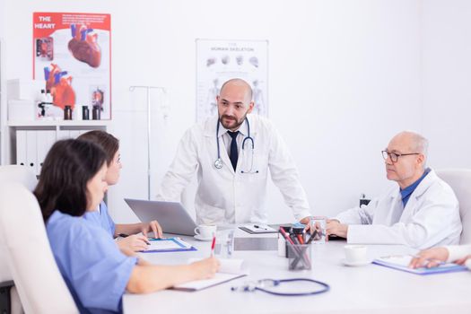 Doctor talking standing and talking with medical staff about treatment for patient. Clinic expert therapist talking with colleagues about disease, medicine professional.