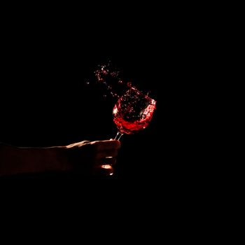 person s hand holding glass red wine splashing out glass. High resolution photo