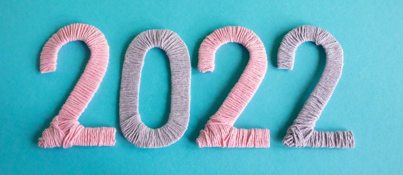 Knitted figures 2022, made of pink and lilac threads, lie on a blue background. The concept of the New Year.