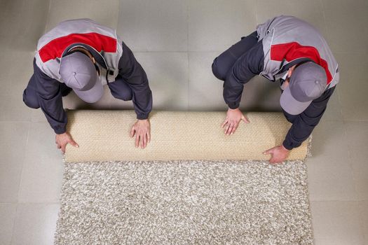 Male Worker Unrolling Carpet On Floor At Home