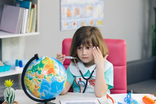 Little kid girl dressed in a doctor's suit measures the temperature of the Earth. Ecology and global warming concept. Earth Temperature with Thermometer Icon for Global Warming and Climate Change
